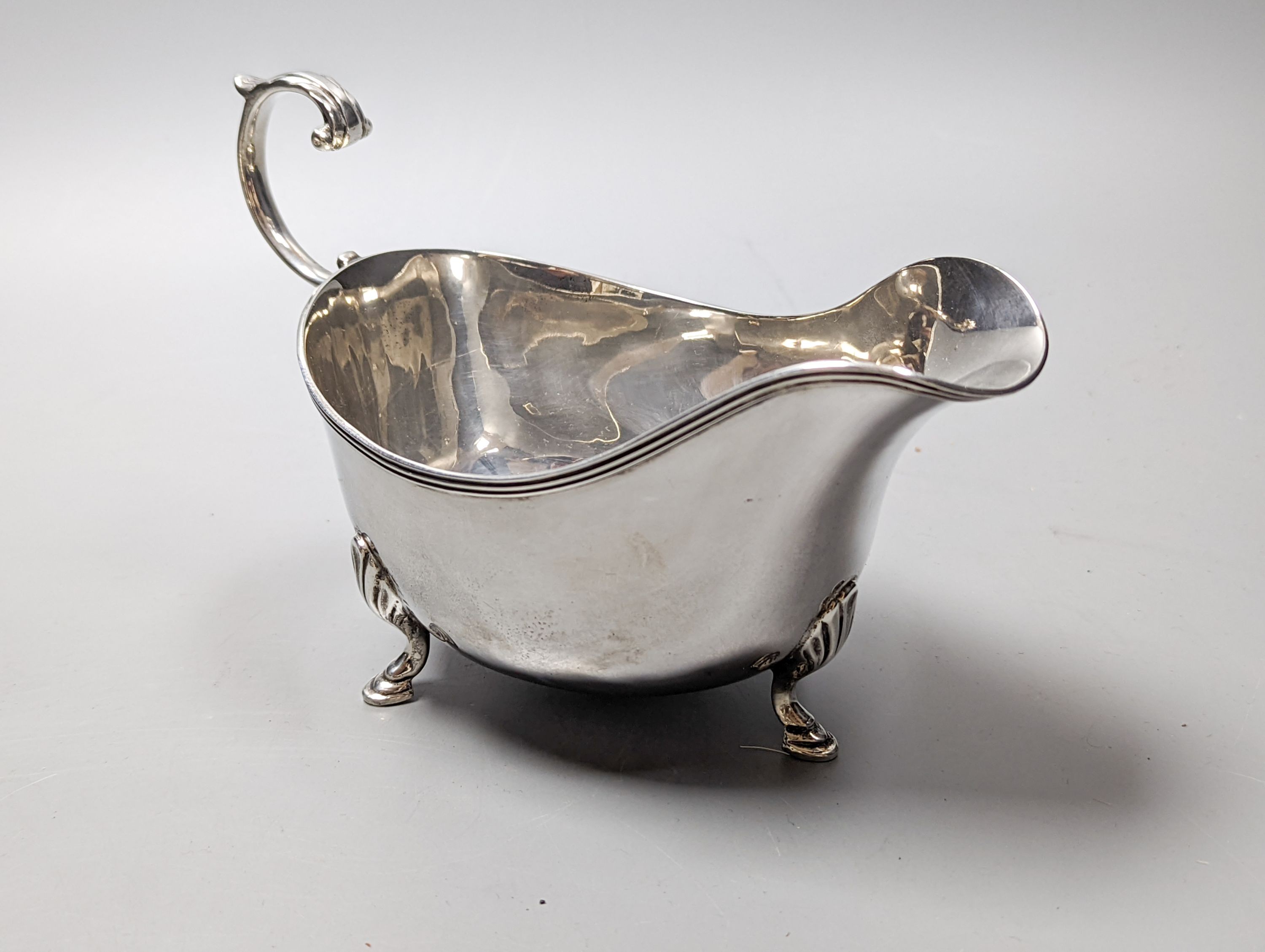 A George V silver sauceboat by Mappin & Webb, Birmingham, 1911, an Edwardian silver tri-handled bowl, a late Victorian repousse silver box and a George V silver sifter spoon, 11oz.